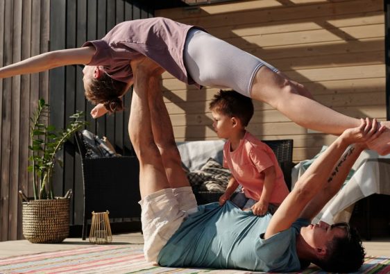 Father and kids doing yoga outdoors on a patio, balancing poses together.