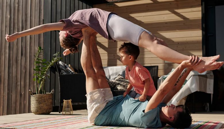 Father and kids doing yoga outdoors on a patio, balancing poses together.